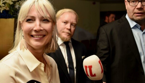 En leende kvinna talar till fler mikrofoner.