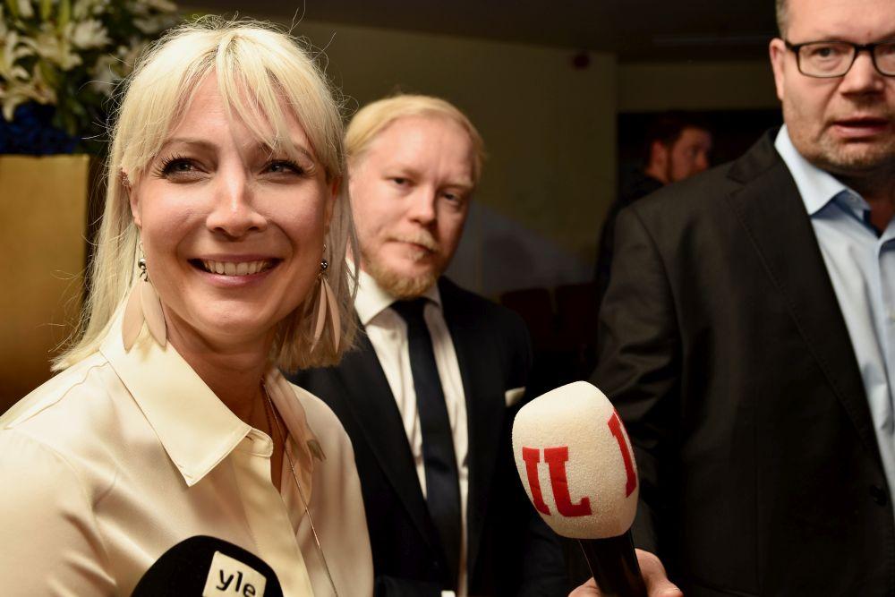 En leende kvinna talar till fler mikrofoner.