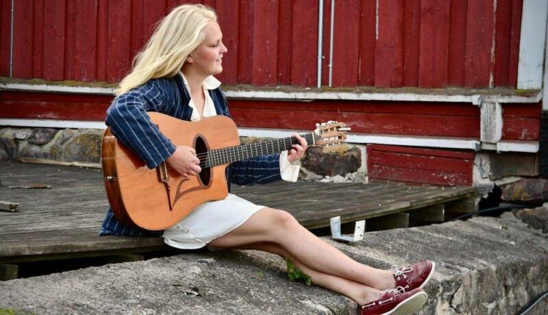 Ung ljushårig kvinna sitter på en klippa med en gitarr i famnen.