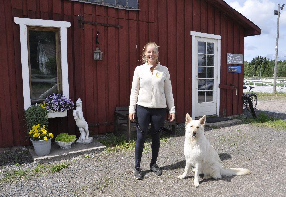 Dam utanför en röd träbyggnad. Bredvid henne sitter en stor ljus hund. 