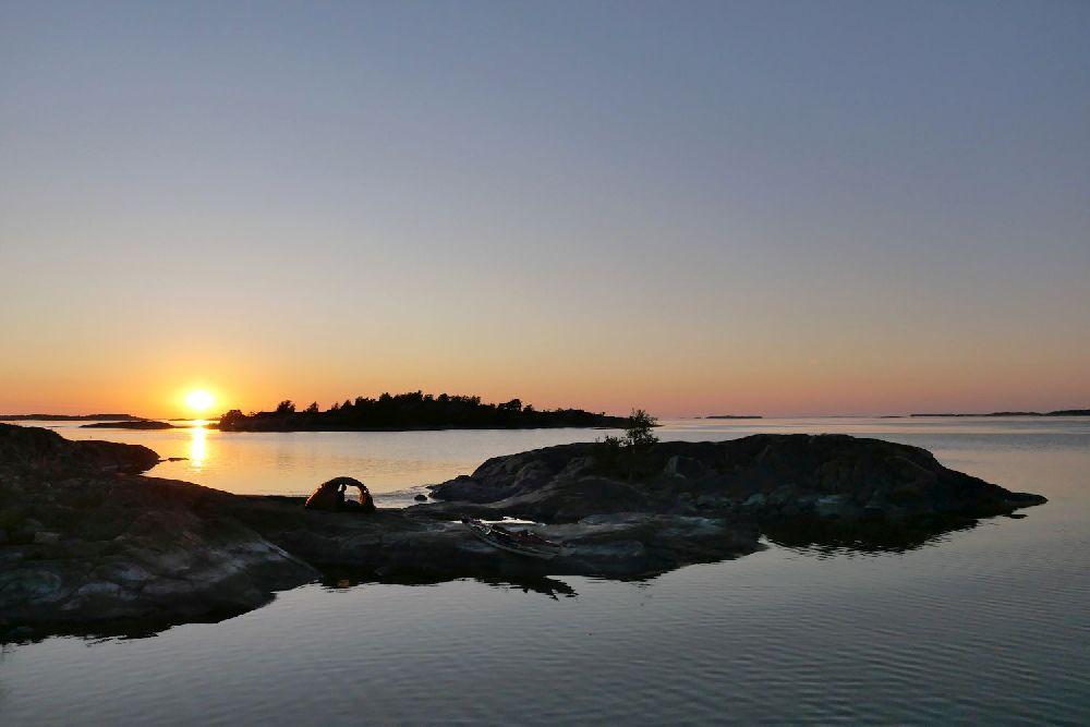 Solnedgång över hav, klippor och ett tält