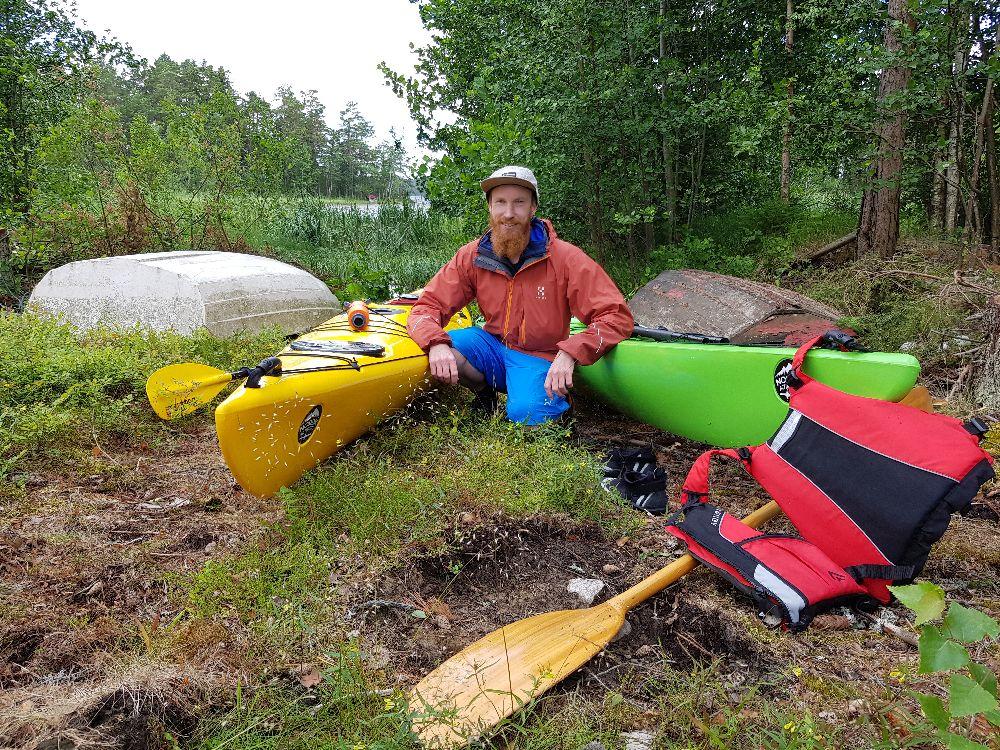 Man sitter på huk utomhus vid två kajaker.
