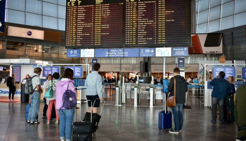 Resenärer står och kollar på skärm med information om avgående flyg på flygfältet.
