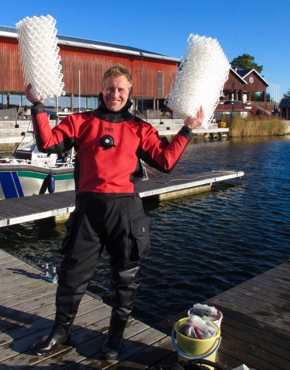 En man klädd i dykardräkt står på en brygga och håller i två block av vitt nät.