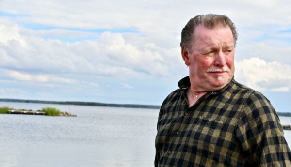 Porträtt av äldre man klädd i flanellskjorta med ett hav i bakgrunden.
