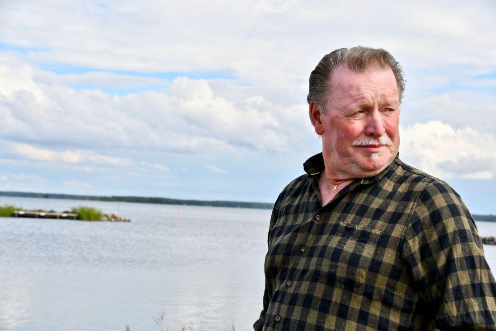 Porträtt av äldre man klädd i flanellskjorta med ett hav i bakgrunden.