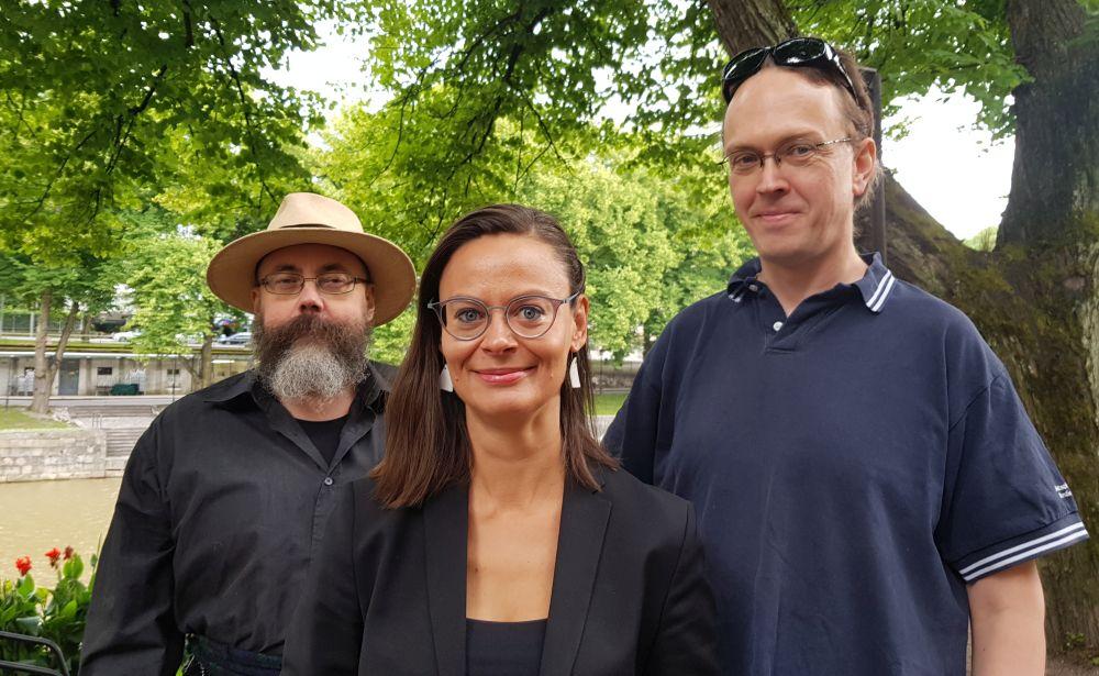 Tre glada personer vid lummig åmiljö
