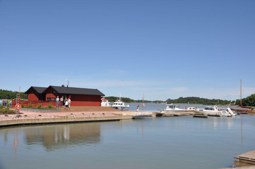 Gästhamn med spegelblankt vatten, några rödmålade hus och båtar.