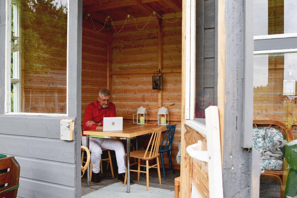 Man med röd skjorta och glasögon vid träväggar.