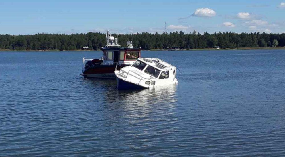 Halvsjunken båt på havet. Bredvid står sjöbevakningens båt.