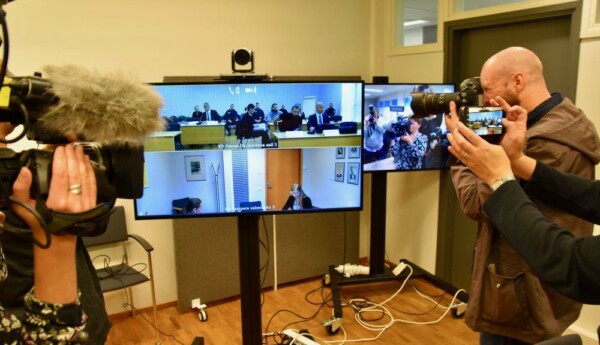 Journalister fotograferar en rättegång via en skärm.