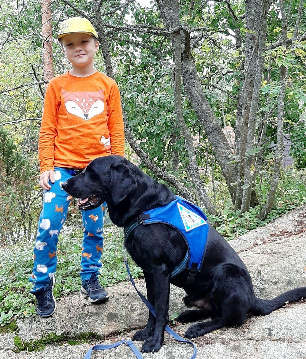 Pojke står vid en sittande hund i en skog