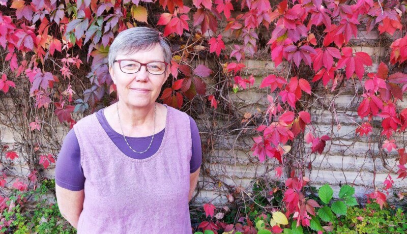 Maria Björkgren-Vikström framför en tegelmur täckt av höströd murgröna.