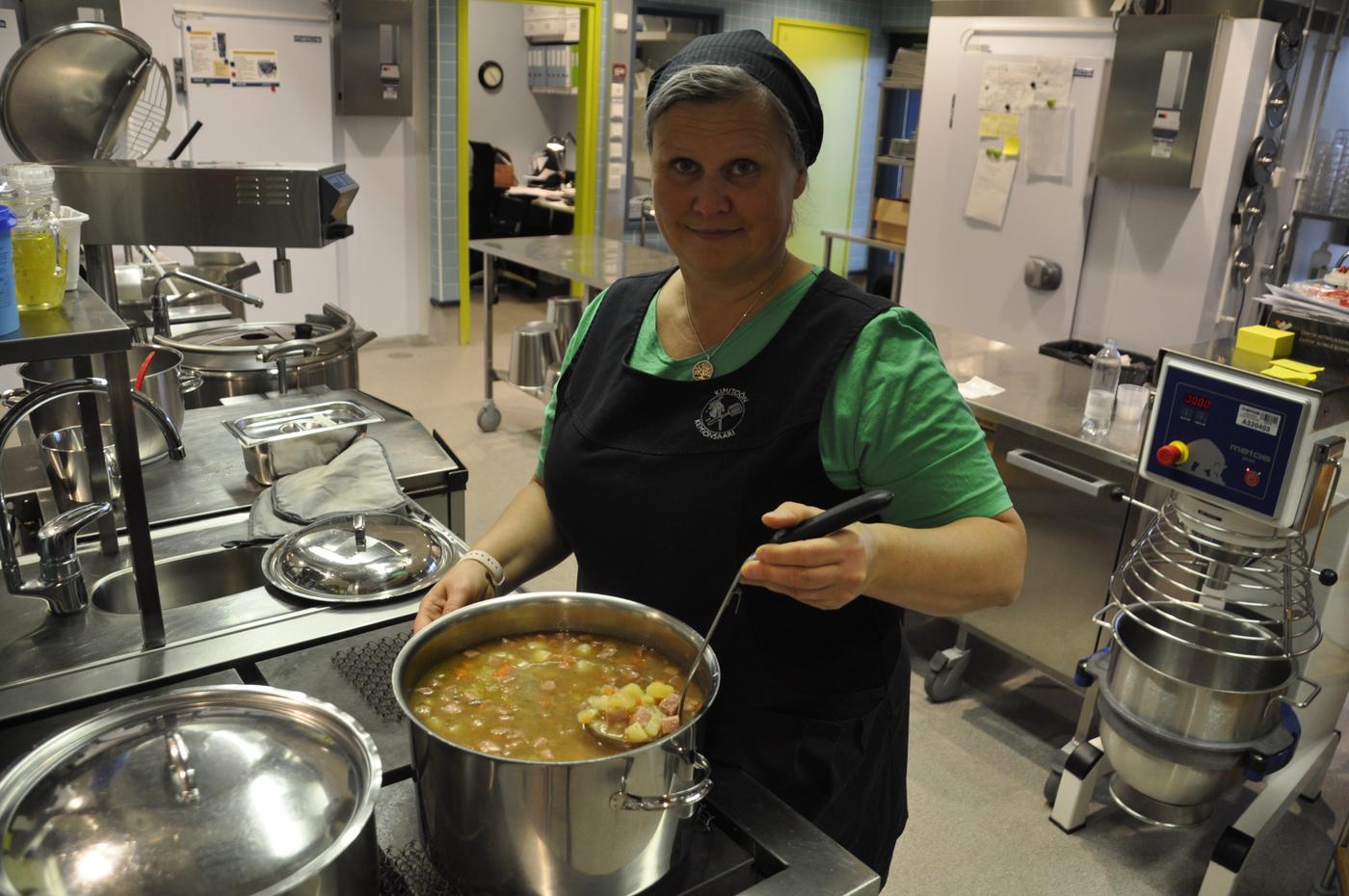 dam i ett skolkök som rör i en kastrull med soppa