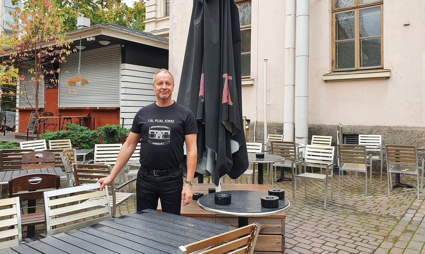 Mika Lattu står bakom ett bord på uteserveringen vid Skolan, med handen på en stolsrygg.