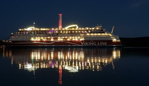 Viking Grace i halvdunkel, med fartygets ljus speglandes i vattenytan.