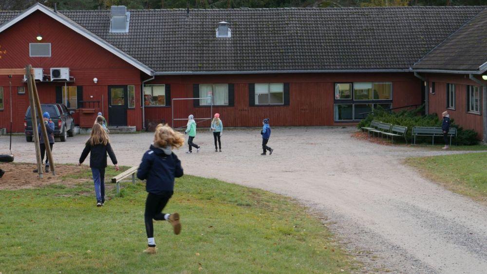 skolelever springer utanför ett rött skolhus