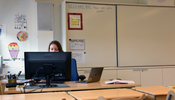 en lärare sitter bakom en datorskärm vid ett skrivbord