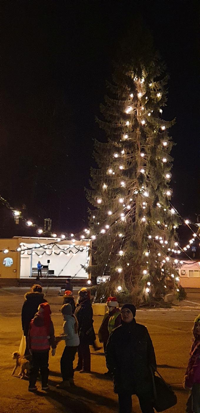 Stor julgran på ett torg. Några personer i förgrunden. 