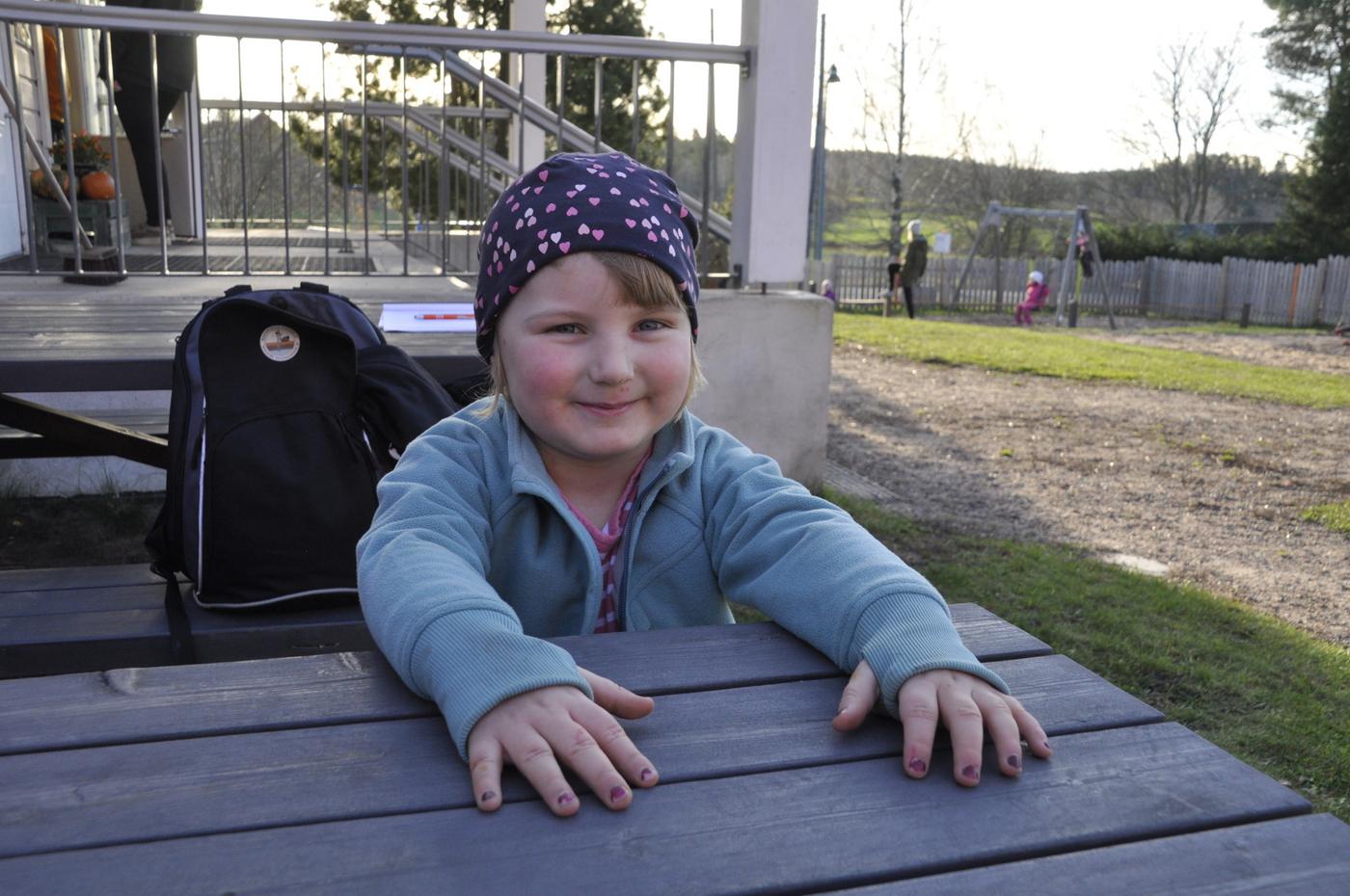 Flicka utomhus, sitter vid ett träbord