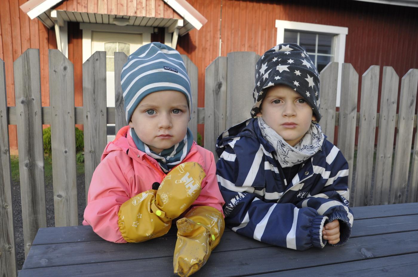 Två små barn sitter vid ett träbord utoomhus.