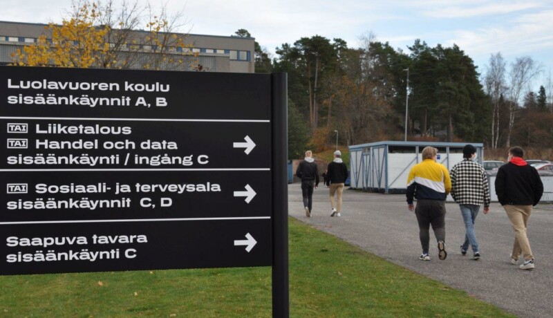 Skylt och studerande framför skolbyggnad