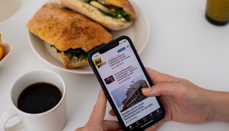 Hand som håller i en mobiltelefon. kaffe och en semla.