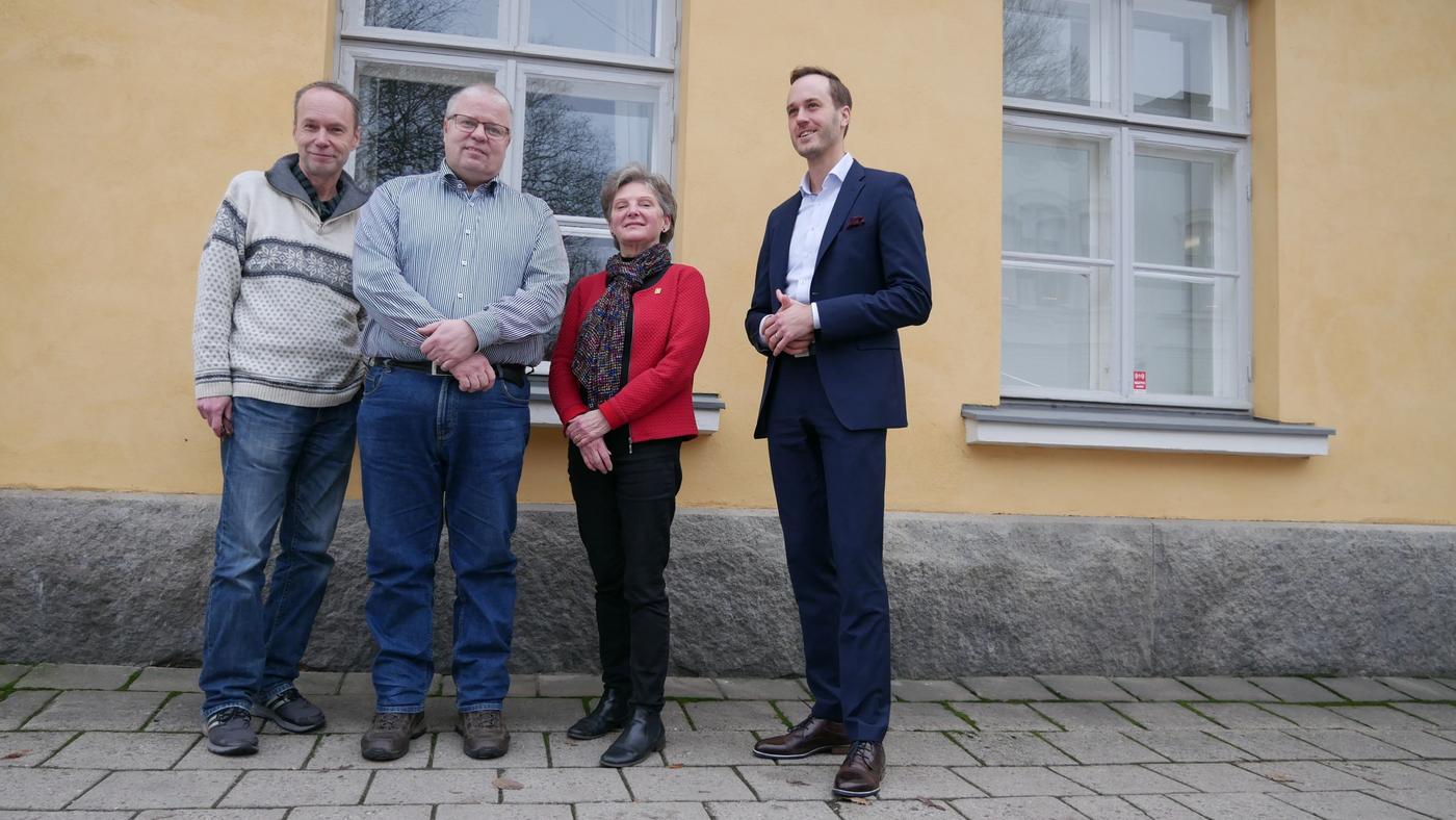 fyra personer poserar för kameran vid en gul yttervägg