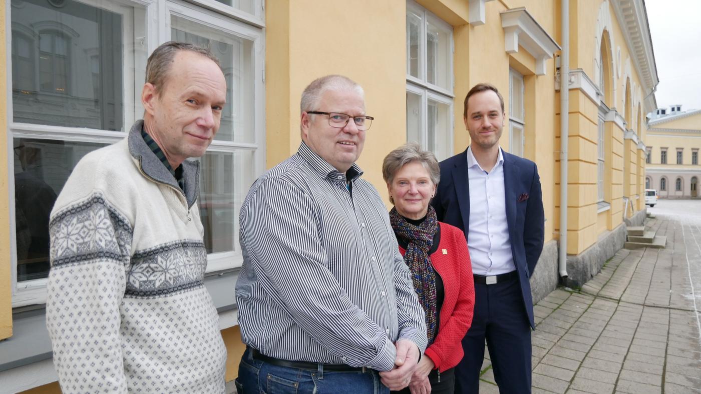 fyra personer poserar för kameran vid en gul yttervägg