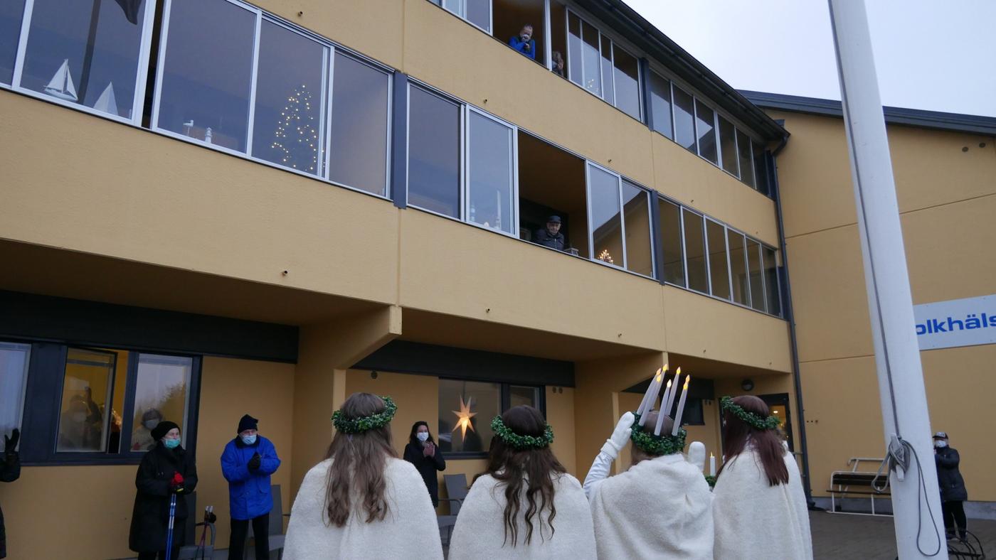 några personer tittar ut från sina balkonger, på marken ett luciatåg