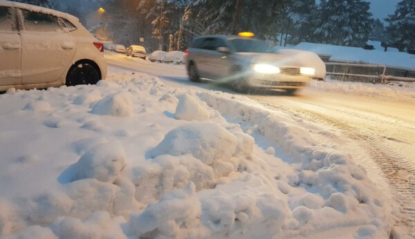 En taxibil som kör i snöyra med en snödriva i förgrunden.