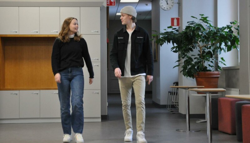 ung kivnna och ung man går leende i en skol-aula
