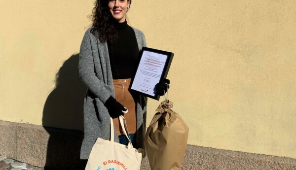 Leende kvinna med blompaket och diplom i handen.