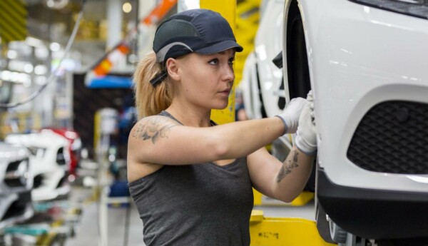 Kvinna som gör något på en bil i en fabrik.