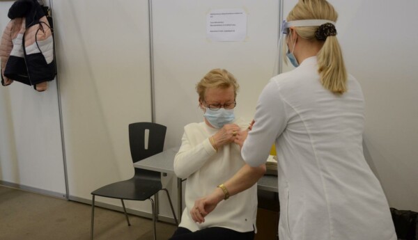 kvinna sitter på en stol och sköterska putsar hennes arm för vaccin