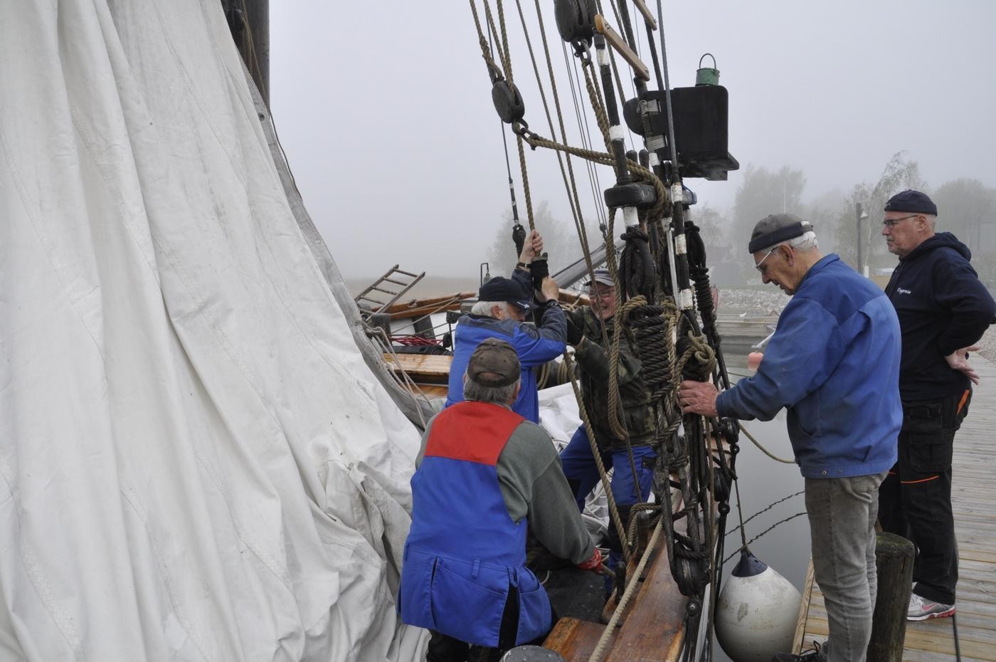 Fem män hissar en segelskutas segel