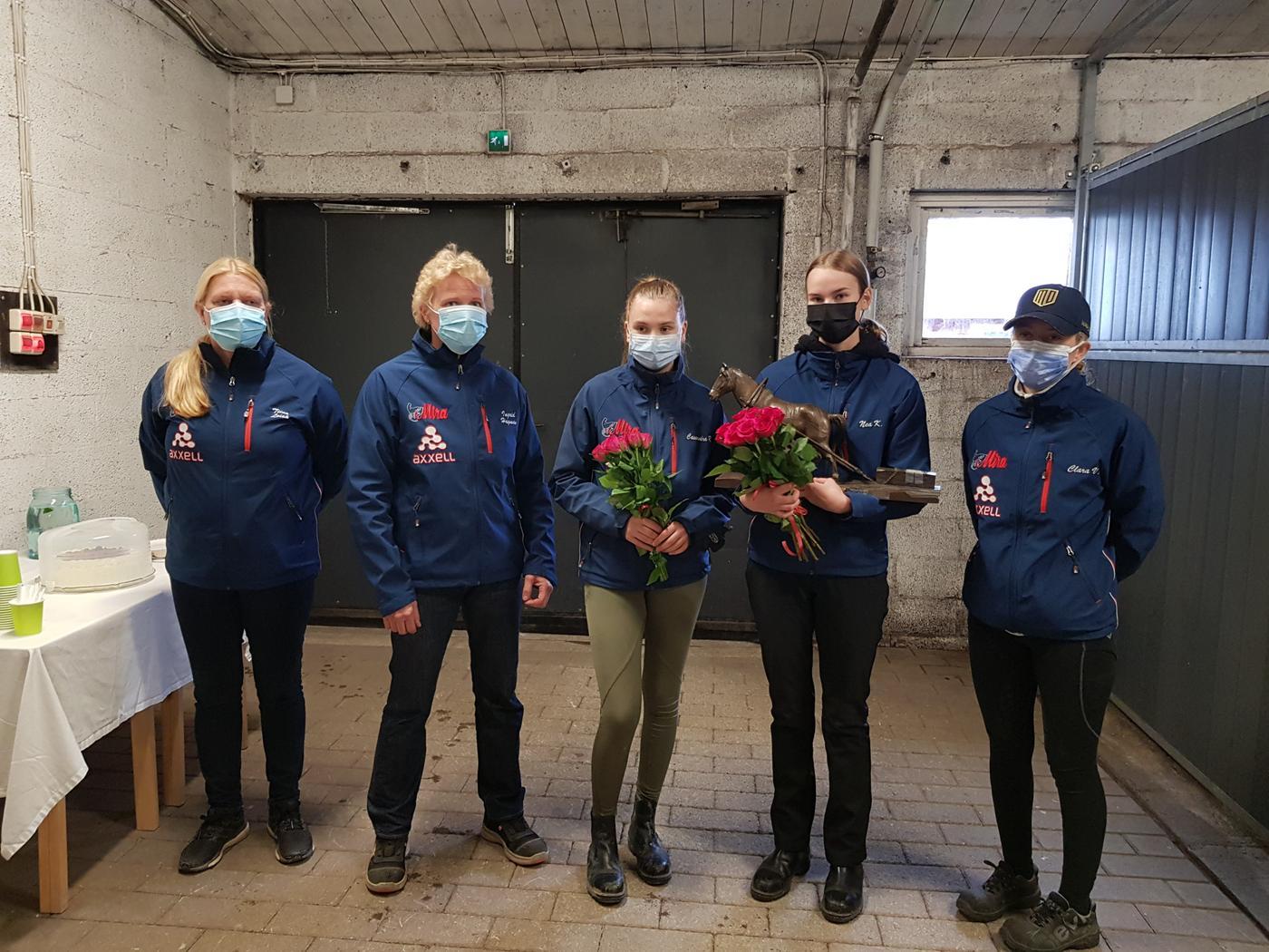 Fem personer på rad i ett stall. Tvp av dem har blommor i handen