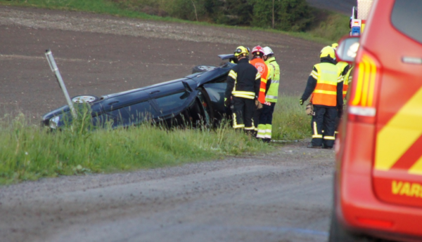 en bil ligger i uppochner i ett dike, räddningspersonal står bredvid