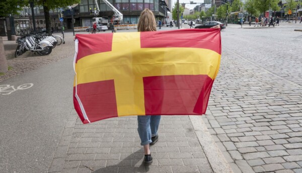 En person håller i en röd flagga med ett gult kors.
