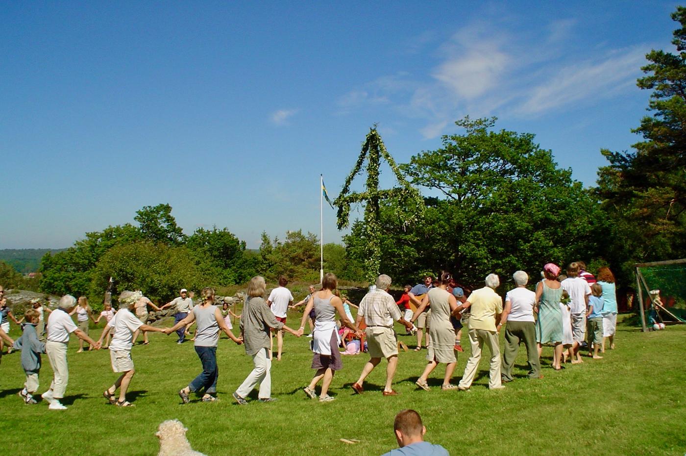 Folk dansar kring en midsommarstång i soligt väder.