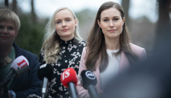 Två kvinnor (Sanna Marin längst fram) står utomhus framför mikrofoner.