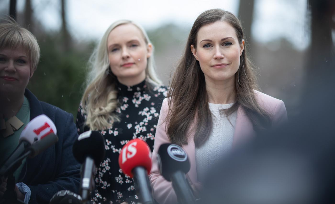 Två kvinnor (Sanna Marin längst fram) står utomhus framför mikrofoner.
