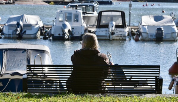 En person sitter på en bänk och blickar ut över en båthamn.