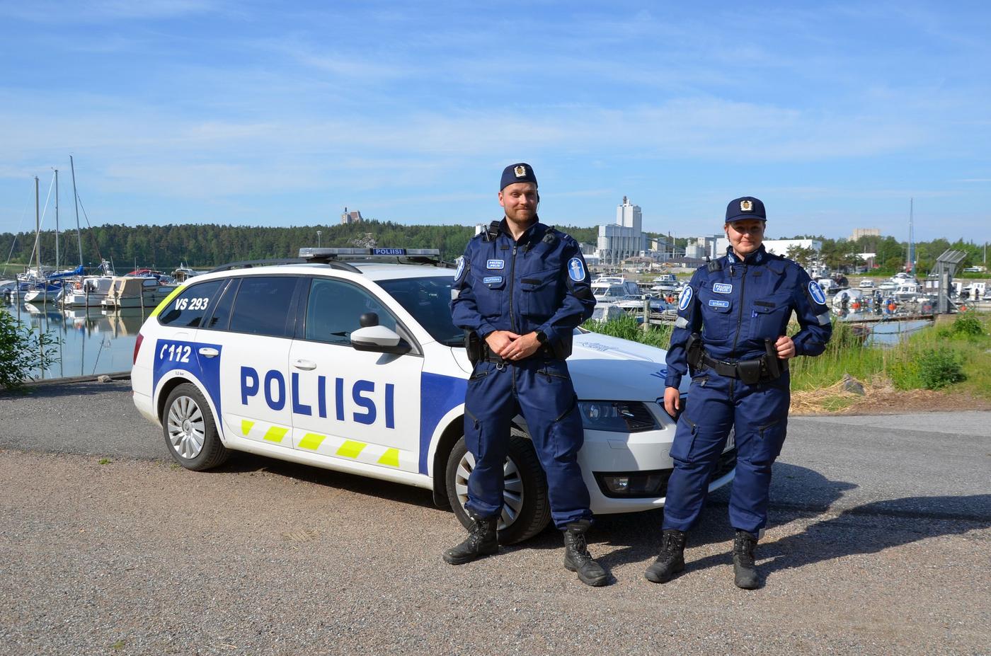 två poliser framför en polisbil i skärgårdsmiljö