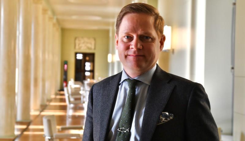 En man iklädd kostym står i en korridor och ler mot kameran.