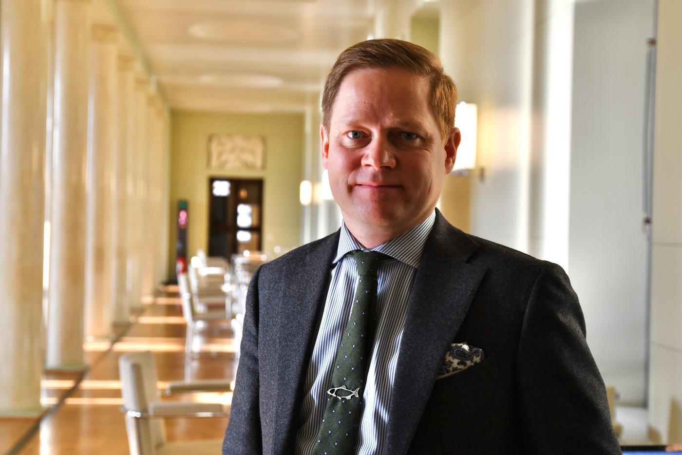 En man iklädd kostym står i en korridor och ler mot kameran.