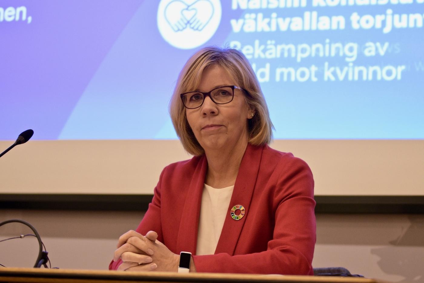 Anna-Maja Henriksson sitter vid ett bord framför en stor skärm.