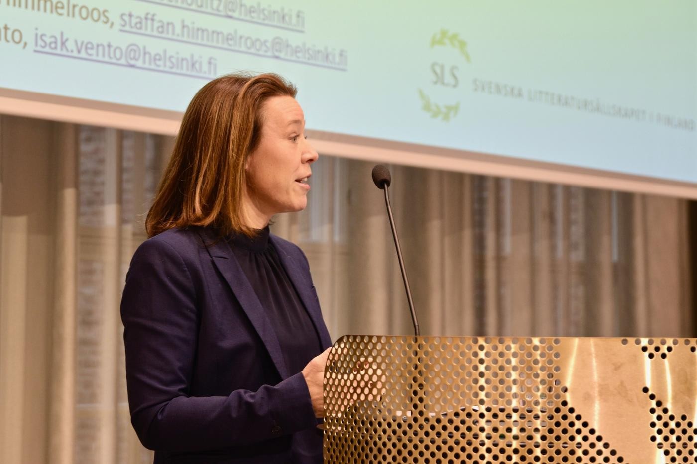 En kvinna står vid ett podium på en scen och talar.