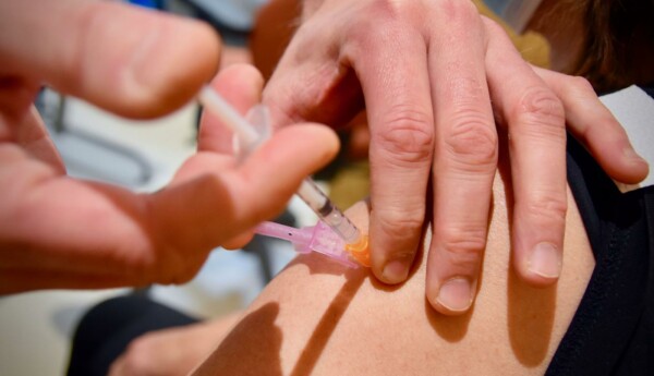 En hand som vaccinerar en överarm.