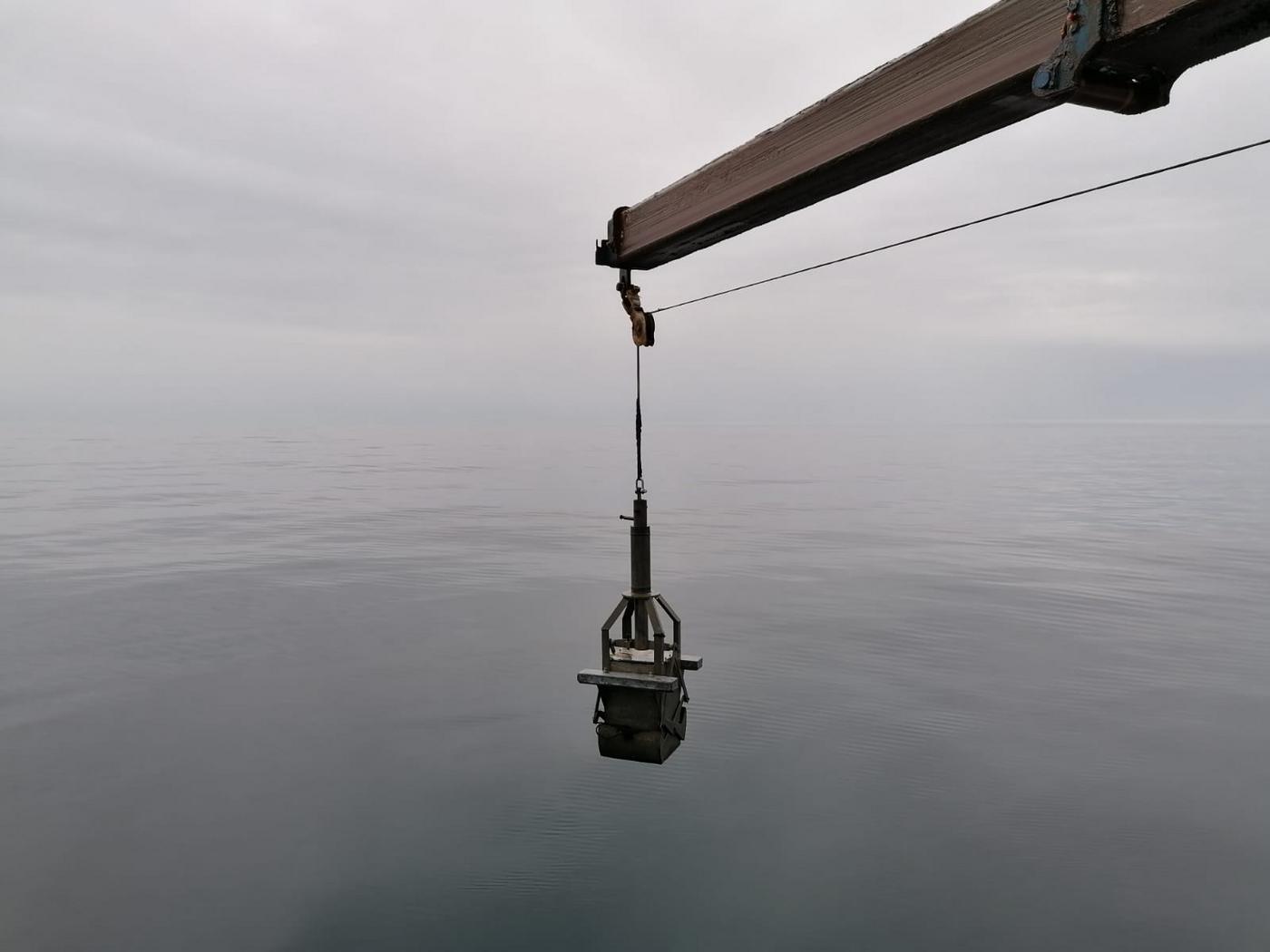 En låda som sänks ner i havet för att ta prover från bottnen. Havsytan är spegelblank.